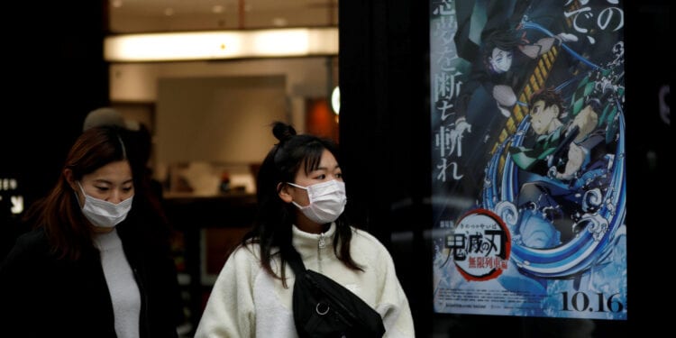 Women masks walk past a poster for the hit Sony-distirbuted animated movie "Demon Slayer" in front of a movie theatre in Tokyo