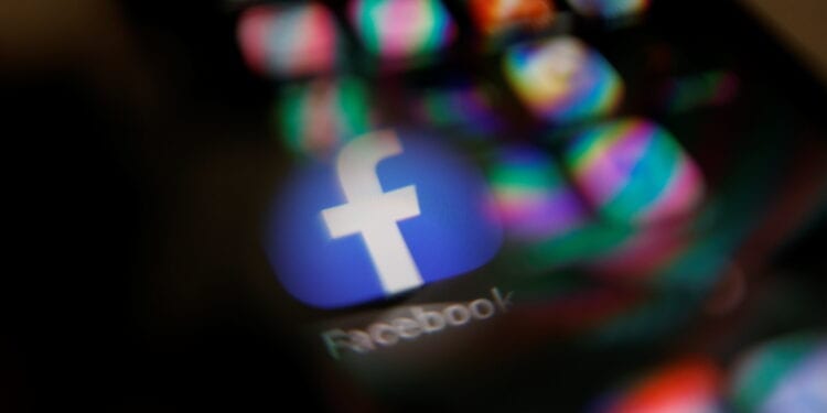 Facebook logo displayed on a mobile phone is seen through a magnifying glass