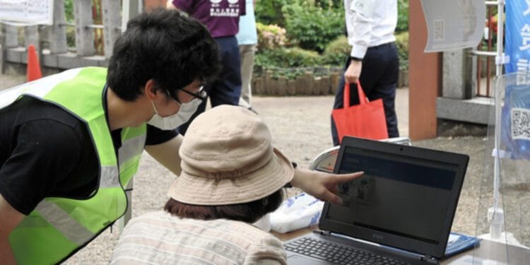 Estudante orienta uma idosa durante evento sobre crimes cibernéticos em Saitama. Reprodução/Jornal Asahi.