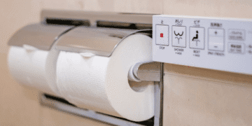 Close-up of a bathroom toilet area showing a wall control panel beside a toilet paper roll holder with a white roll.