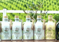 Row of olive oil bottles with olive tree branding arranged on a table against a green field backdrop