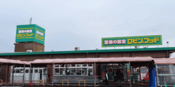 Storefront with green signs and Japanese text, pink canopy over cart area, several people near the entrance.