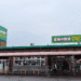 Storefront with green signs and Japanese text, pink canopy over cart area, several people near the entrance.