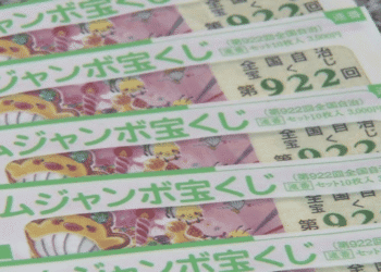 Row of colorful Japanese lottery tickets with green text and cartoon characters, stacked on a speckled surface. The tickets show a yellow mascot and playful illustrations.