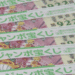 Row of colorful Japanese lottery tickets with green text and cartoon characters, stacked on a speckled surface. The tickets show a yellow mascot and playful illustrations.