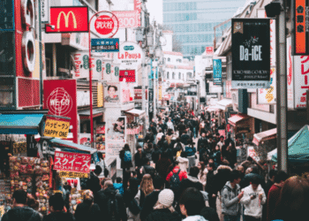Crowded shopping street in Tokyo with colorful neon signs and storefronts on both sides.