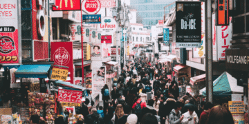 Crowded shopping street in Tokyo with colorful neon signs and storefronts on both sides.