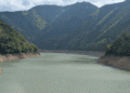 Calm river or reservoir winding through a forested mountain valley with steep slopes on either side.