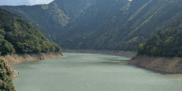 Restrições de água são reduzidas na província de Aichi após recuperação de barragens - ThingsOut Calm river or reservoir winding through a forested mountain valley with steep slopes on either side.