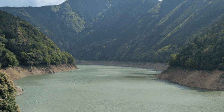 Restrições de água são reduzidas na província de Aichi após recuperação de barragens - ThingsOut Calm river or reservoir winding through a forested mountain valley with steep slopes on either side.