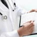 Seguro contra incapacidade cresce como proteção de renda no Japão - ThingsOut Doctor wearing a white coat and stethoscope writes on a medical form on a clipboard.
