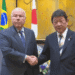 Brasil e Japão ampliam diálogo econômico com foco em energia comércio e cooperação estratégica - ThingsOut Two men in suits shake hands in a formal meeting room with Brazil and Japan flags behind them.