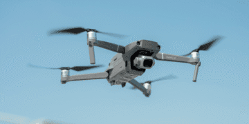 Drone in midair: a gray Mavic 2 quadcopter with forward-facing camera against a blue sky, propellers blurred from motion.
