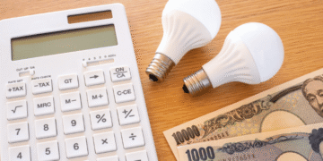 Japão amplia subsídios de luz e gás no verão para aliviar contas das famílias - ThingsOut Calculator with two white bulbs and 1,000-yen banknotes on a wooden desk.
