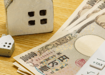 Money and house models on a wooden desk with a calculator, suggesting mortgage or real estate financing.