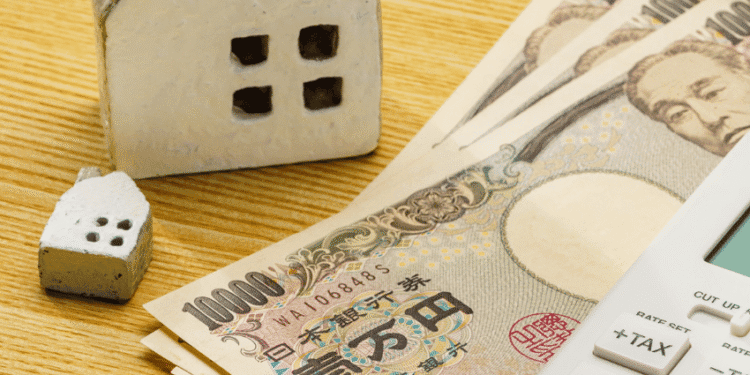 Money and house models on a wooden desk with a calculator, suggesting mortgage or real estate financing.