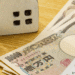 Money and house models on a wooden desk with a calculator, suggesting mortgage or real estate financing.