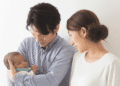 Young couple gently cradle their newborn baby, looking at the infant with affection in a bright room.