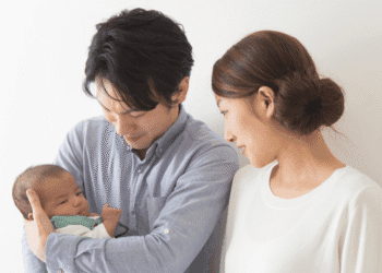 Young couple gently cradle their newborn baby, looking at the infant with affection in a bright room.