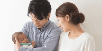 Young couple gently cradle their newborn baby, looking at the infant with affection in a bright room.