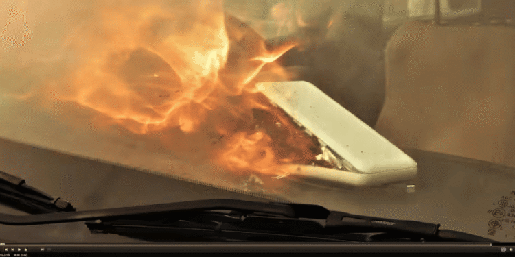 Fire seen inside a vehicle through the windshield, engulfing a white rectangular object on the passenger side.