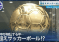 News broadcast screenshot showing a large gold metallic soccer ball with Japanese captions about a colossal ball