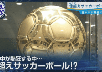 News broadcast screenshot showing a large gold metallic soccer ball with Japanese captions about a colossal ball