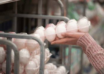 Person selecting a carton of white eggs from a store display shelf.