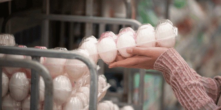 Person selecting a carton of white eggs from a store display shelf.