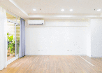 Bright empty living room with wood floor, white walls, recessed lighting, and a sliding glass door with purple curtains.