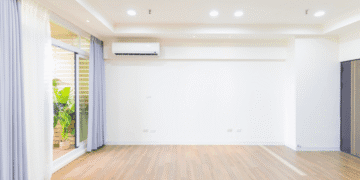 Bright empty living room with wood floor, white walls, recessed lighting, and a sliding glass door with purple curtains.