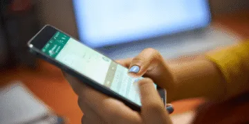 Golpe no WhatsApp usa SMS falso para assustar usuários e tentar roubar códigos de verificação - ThingsOut Person typing on a smartphone while a laptop sits blurred in the background.