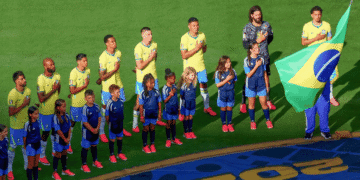 Hino Nacional do Brasil é eleito o mais bonito entre os 48 países da Copa pelo The New York Times - ThingsOut Brazil national team players and children stand in line with hands over their hearts on a soccer pitch, a flag bearer holding the Brazilian flag nearby