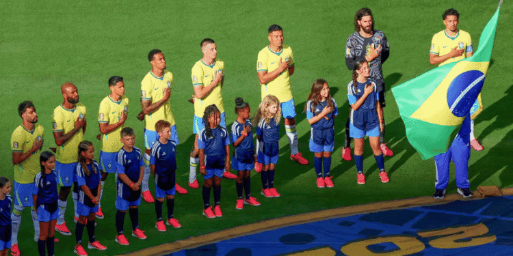 Hino Nacional do Brasil é eleito o mais bonito entre os 48 países da Copa pelo The New York Times - ThingsOut Brazil national team players and children stand in line with hands over their hearts on a soccer pitch, a flag bearer holding the Brazilian flag nearby