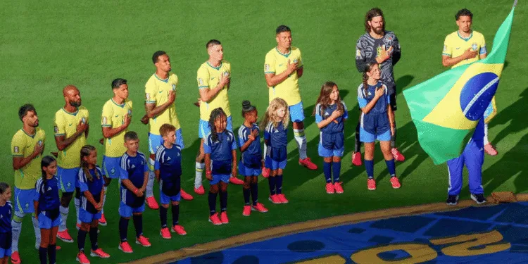 Hino Nacional do Brasil é eleito o mais bonito entre os 48 países da Copa pelo The New York Times - ThingsOut Brazil national team players and children stand in line with hands over their hearts on a soccer pitch, a flag bearer holding the Brazilian flag nearby