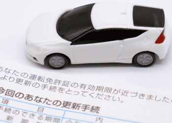 White toy car resting on a Japanese vehicle license renewal document.