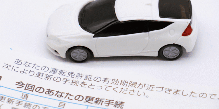 White toy car resting on a Japanese vehicle license renewal document.