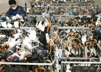 Man wearing a mask sorts through a crowded rack of umbrellas tagged with labels in a storage room.