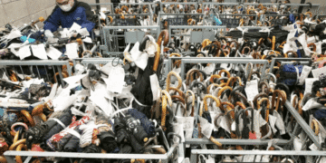 Man wearing a mask sorts through a crowded rack of umbrellas tagged with labels in a storage room.