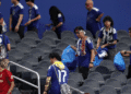 Torcida japonesa reforça tradição de limpeza e chama atenção após empate na Copa - ThingsOut Fans in blue jerseys walk through grey stadium seats, carrying blue bags and scarves, some with face paint.