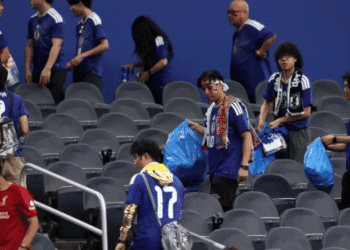 Fans in blue jerseys walk through grey stadium seats, carrying blue bags and scarves, some with face paint.