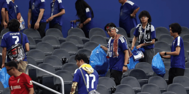 Torcida japonesa reforça tradição de limpeza e chama atenção após empate na Copa - ThingsOut Fans in blue jerseys walk through grey stadium seats, carrying blue bags and scarves, some with face paint.