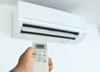 Hand holding a remote control aimed at a wall-mounted air conditioner unit above.
