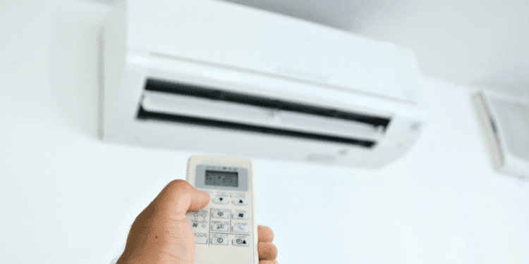 Hand holding a remote control aimed at a wall-mounted air conditioner unit above.