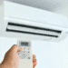 Hand holding a remote control aimed at a wall-mounted air conditioner unit above.