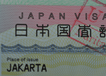 Close-up of a Japan visa card showing 'JAPAN VISA' and 'Place of issue JAKARTA' visible behind a decorative background.