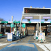 Highway toll plaza in Japan with multiple ETC lanes and green signs; digital board overhead and a 20 km/h speed limit sign visible in the foreground.