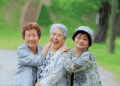 Three elderly women smiling and embracing each other in a green park.