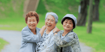 Japão prevê queda nas contas de luz e gás em agosto com reforço de subsídios 1 - ThingsOut Three elderly women smiling and embracing each other in a green park.