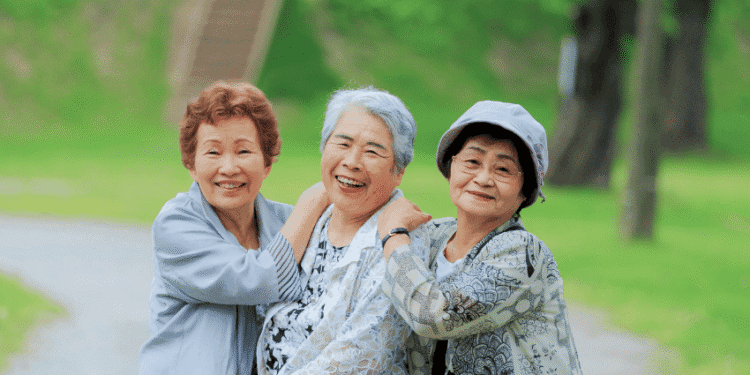 Japão prevê queda nas contas de luz e gás em agosto com reforço de subsídios 1 - ThingsOut Three elderly women smiling and embracing each other in a green park.
